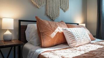 A neatly made bed with a wooden headboard, two bedside lamps, and macramé wall hangings.