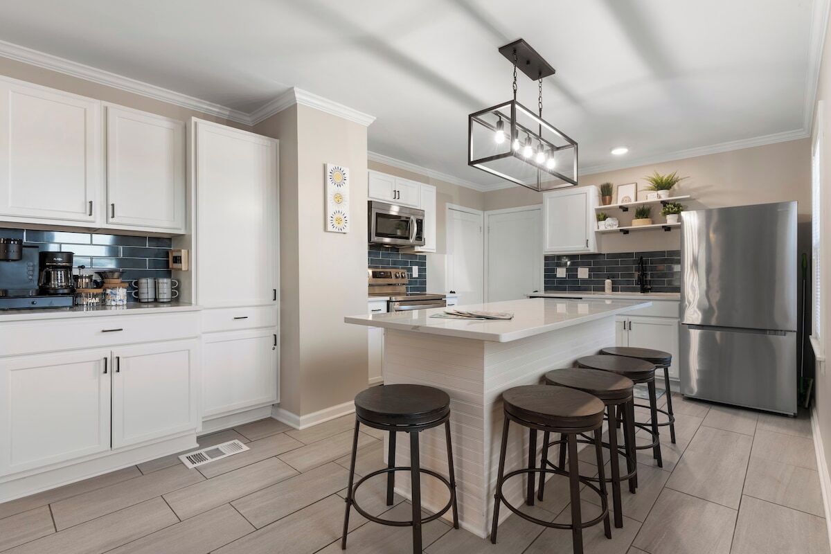 A modern kitchen with white cabinets, a stainless steel refrigerator, and a bar area with stools.