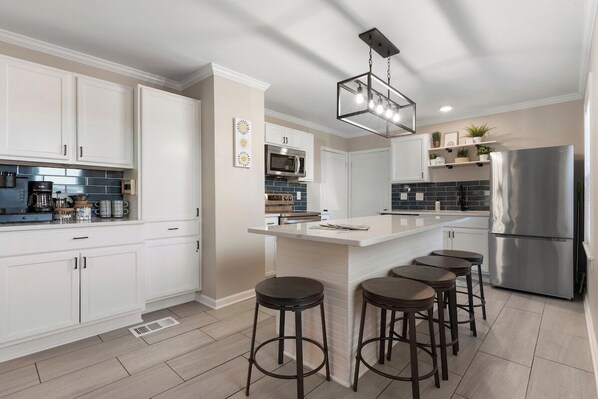 Una cocina moderna con armarios blancos, un refrigerador de acero inoxidable y una zona de bar con taburetes.