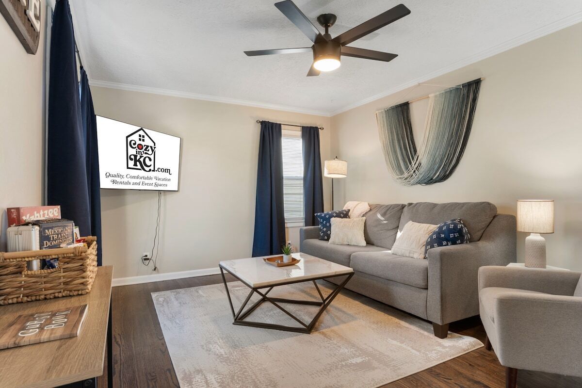 A living room with a sofa, a coffee table, a ceiling fan, and a wall-mounted TV displaying a rental service.