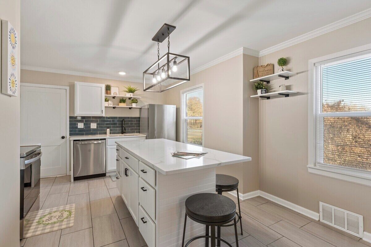 A modern kitchen with a central island, stainless steel appliances, and a window with blinds.