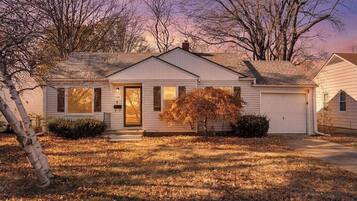 A single-story house with a front door, a garage, and a small front yard with a tree.