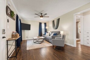 A living room with a sofa, a coffee table, a TV, and a ceiling fan. - The Sunnyside- Waldo Ranch + Fenced Yard + Parking (Kansas City)