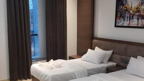 Una habitación de hotel con dos camas, un ventilador de techo, un ventanal con cortinas y un cuadro en la pared.
