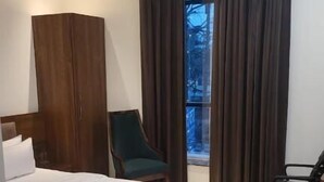 Un dormitorio con cama, una silla, un escritorio, un armario, una ventana con cortinas y un ventilador de techo.