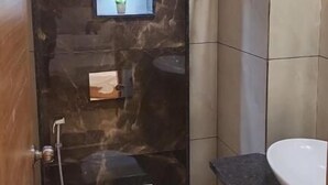 Un baño con pared de mármol, un inodoro, un lavamanos y una ducha.