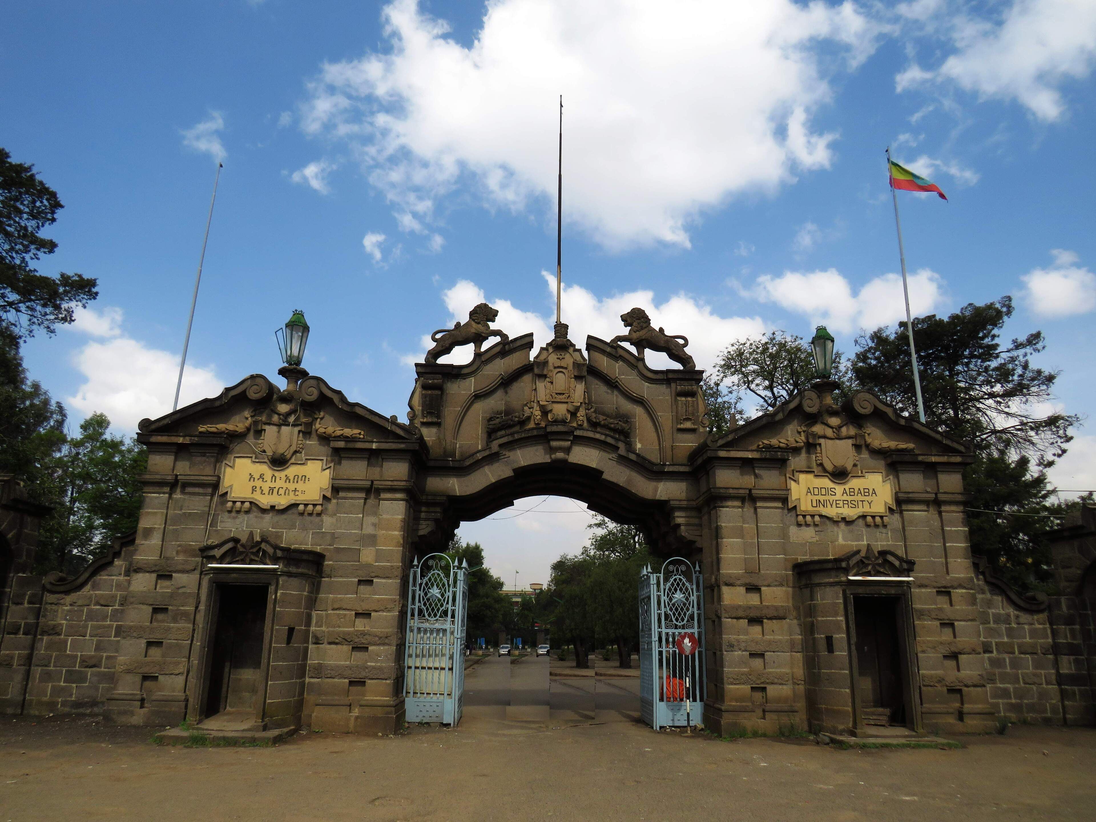 Un arc en pierre d’époque, surmonté de statues de lions, et flanqué de deux portails avec des panneaux indicateurs.
