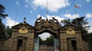 Un arc en pierre d’époque, surmonté de statues de lions, et flanqué de deux portails avec des panneaux indicateurs.