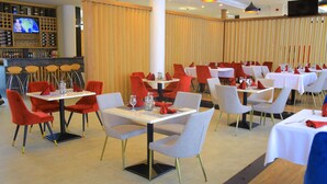 A restaurant with multiple tables and chairs, a bar area with a TV, and a wooden partition wall.