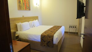 A hotel room with a bed, a TV mounted on the wall, a painting on the wall, and a wooden floor.