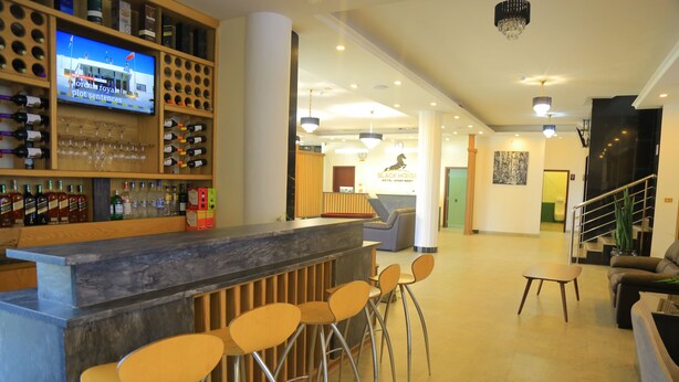 A hotel lobby with a bar area, wooden chairs, a reception desk, and a television screen.
