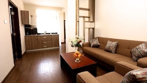 A living room with a sofa, a coffee table with fruit, and a kitchen in the background.