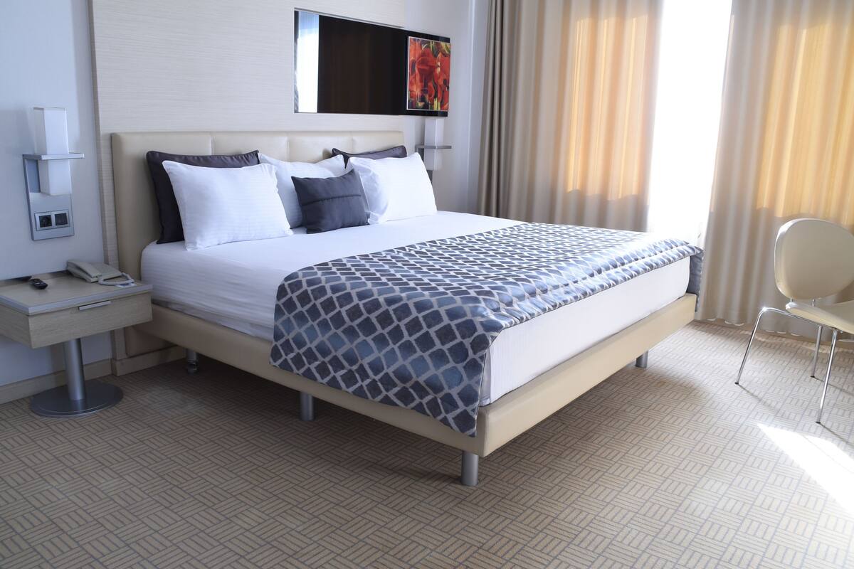 Una habitación de hotel con cama, mesita de noche con teléfono, silla y televisor montado en la pared.