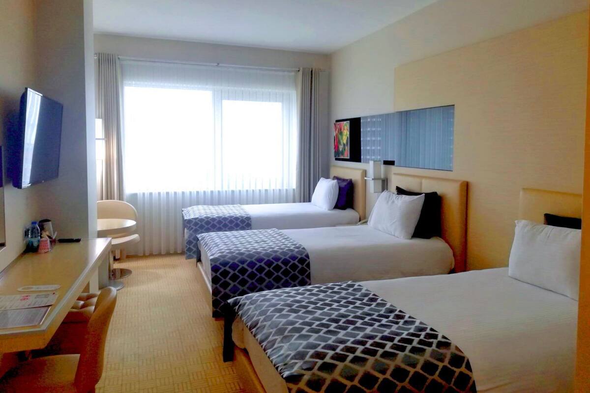 Habitación de hotel con dos camas, un escritorio, una silla, un televisor y una ventana con cortinas.