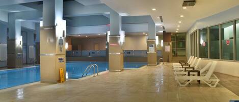 A swimming pool area with lounge chairs and a tiled floor.