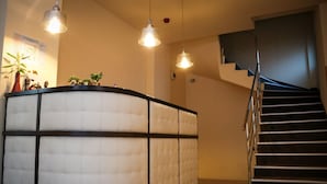 Un vestíbulo de hotel con una recepción, una escalera e iluminación colgante.