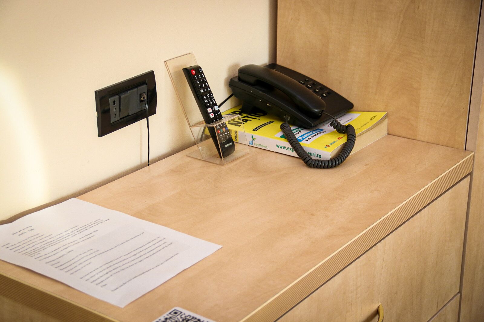 A wooden desk with a telephone, a remote control, and a box of tissues.