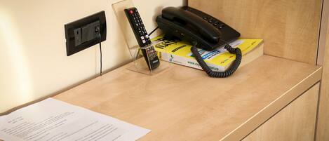 A wooden desk with a telephone, a remote control, and a box of tissues.