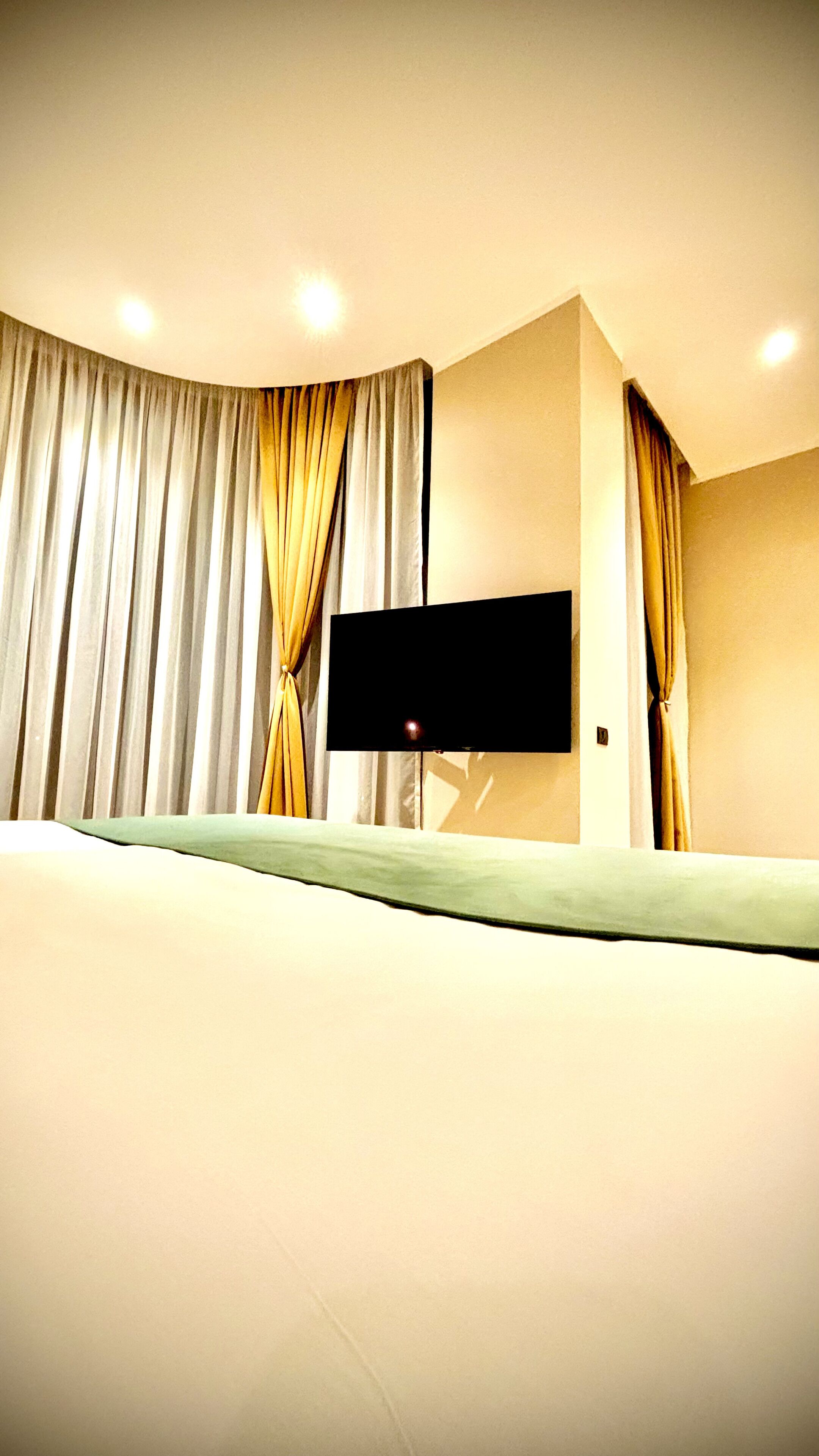 A hotel room with a bed, curtains, a flat-screen TV, and a ceiling light.