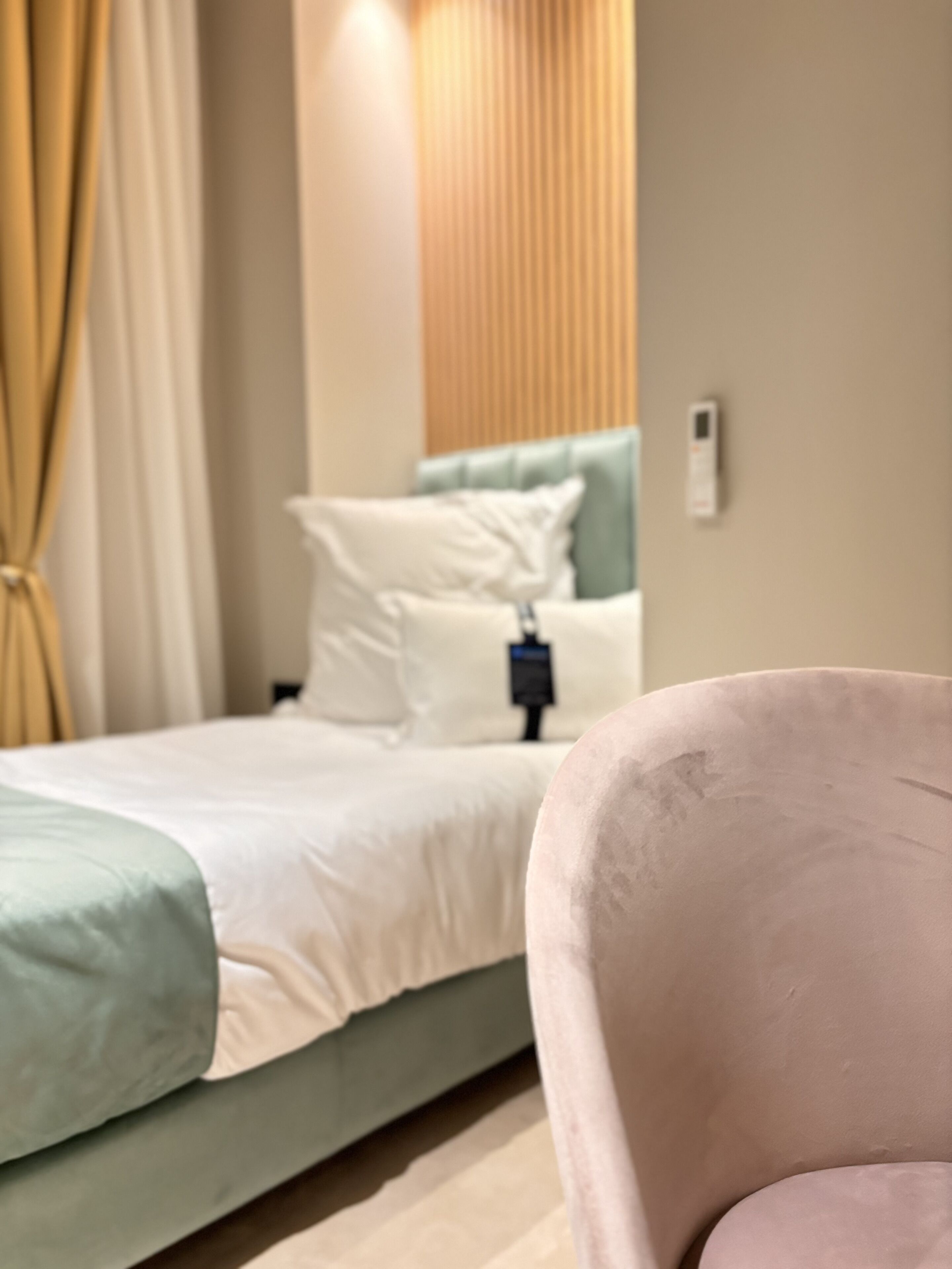 A bed with a green and white bedspread, a white pillow, and a headboard with vertical lines. There is a power outlet on the wall.