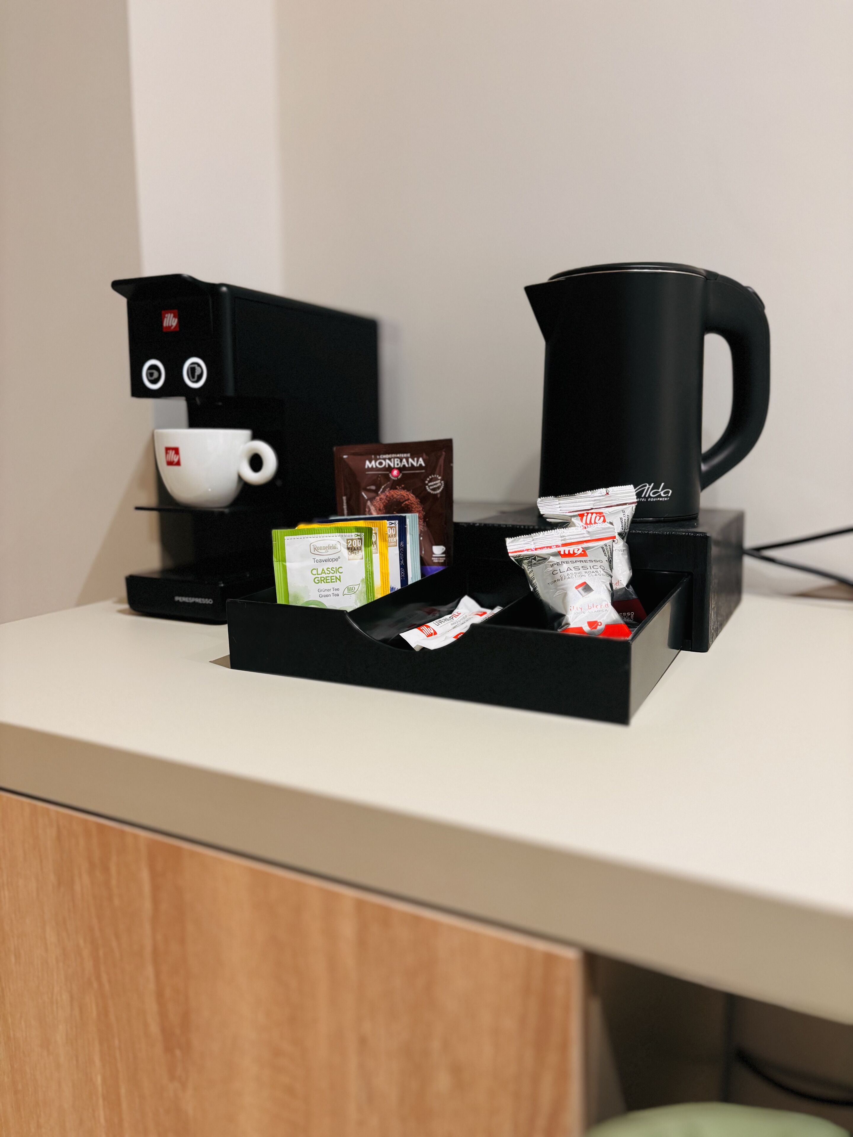 Una estación de café con cafetera, taza y diferentes cápsulas de café.