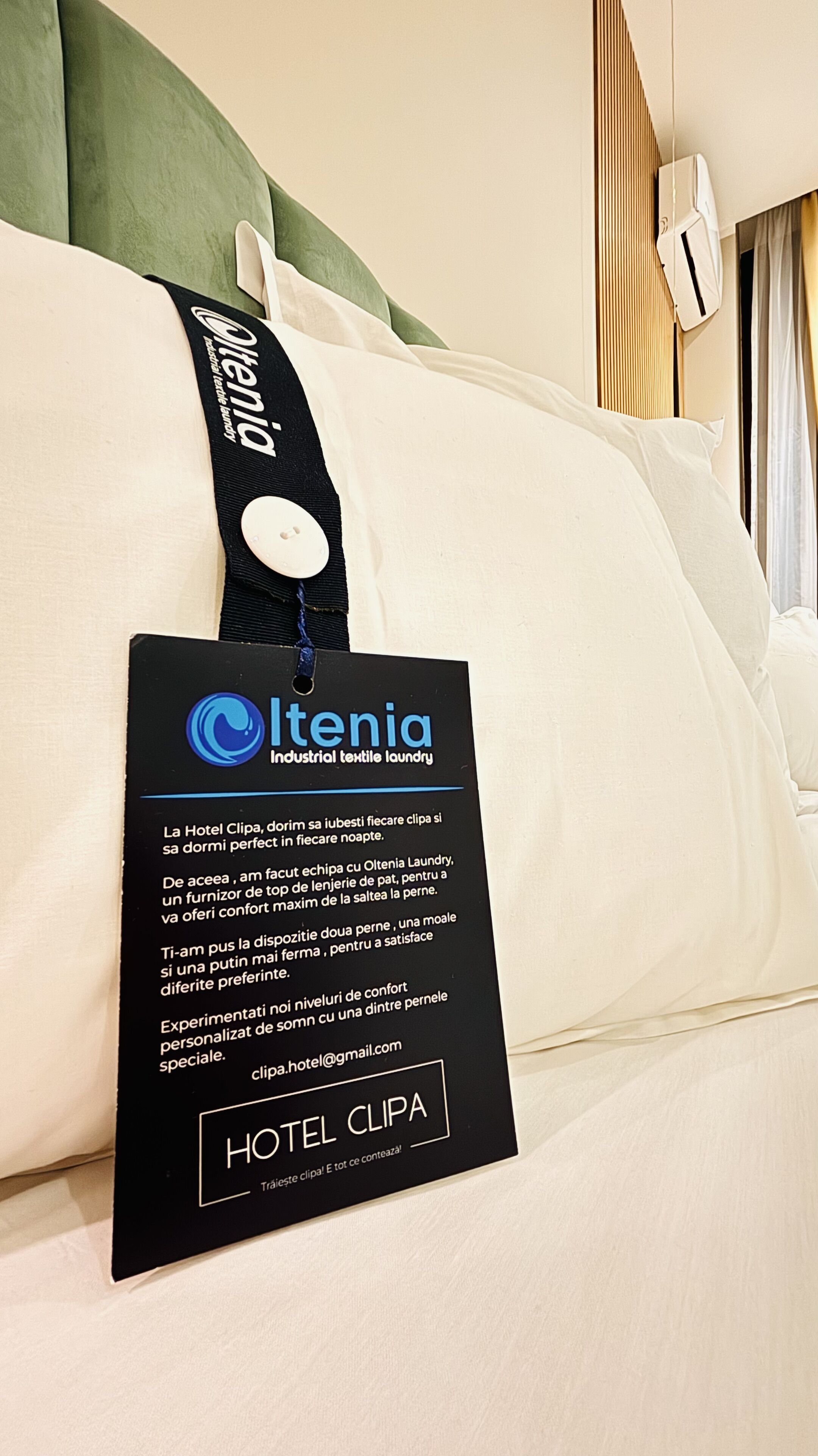 Een hotelbed met een kussen waarop 'Olenia Industrieel textielwasserij' staat.