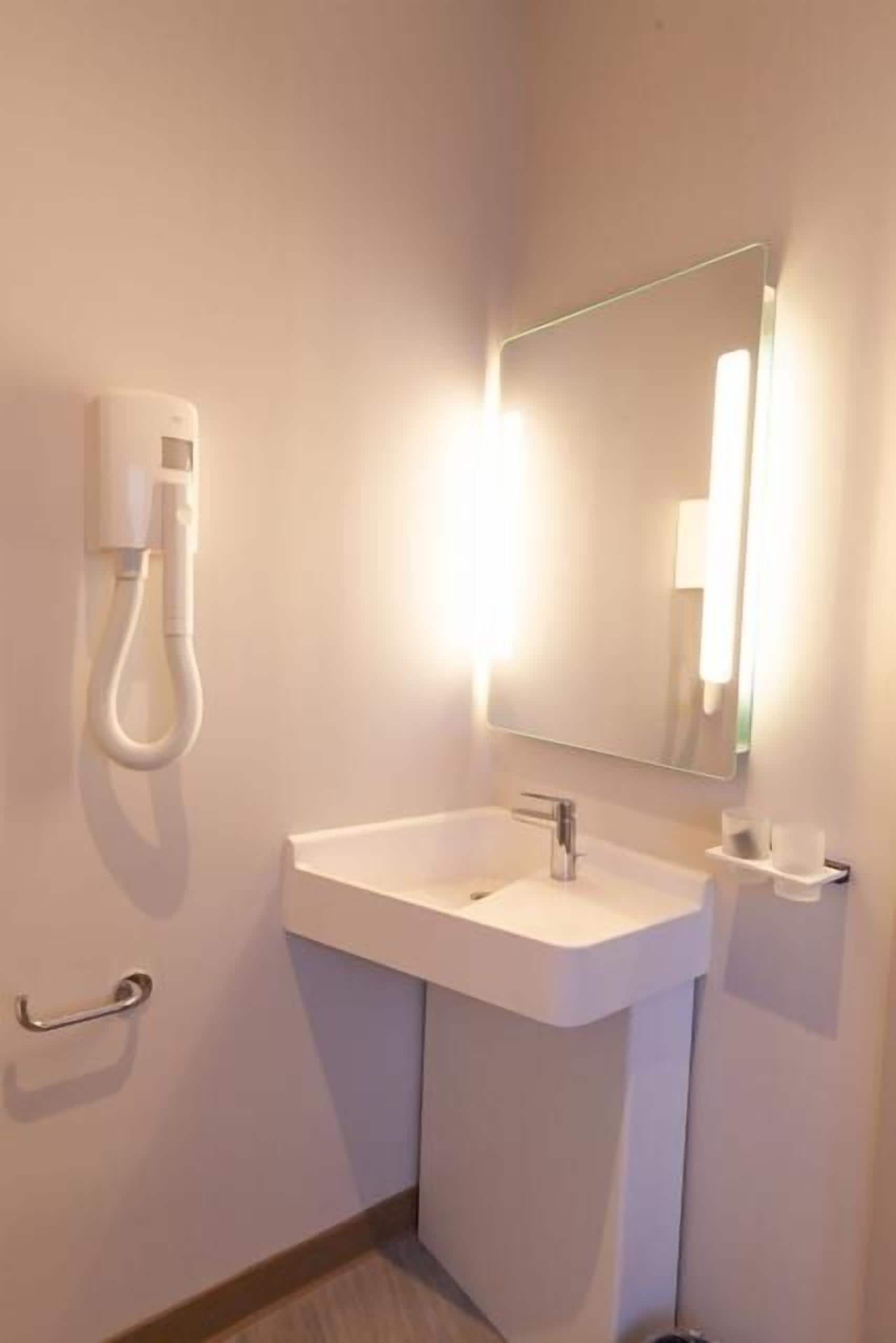 A bathroom with a white sink, a mirror, and a hand dryer.