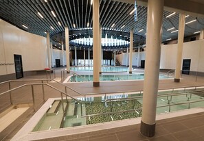 A spacious indoor swimming pool with multiple lanes, surrounded by a modern architectural design with large pillars and a high ceiling. - HNG Hotel Nancy Gare (Nancy)
