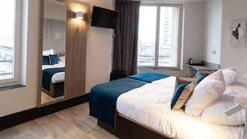 A hotel room with a bed, a TV, a desk, and a view of the city.