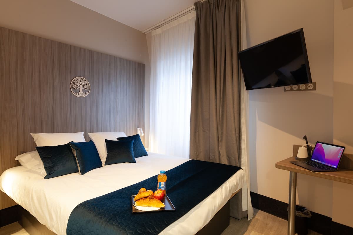 A hotel room with a bed, a laptop on a side table, and a fruit tray on the bed.