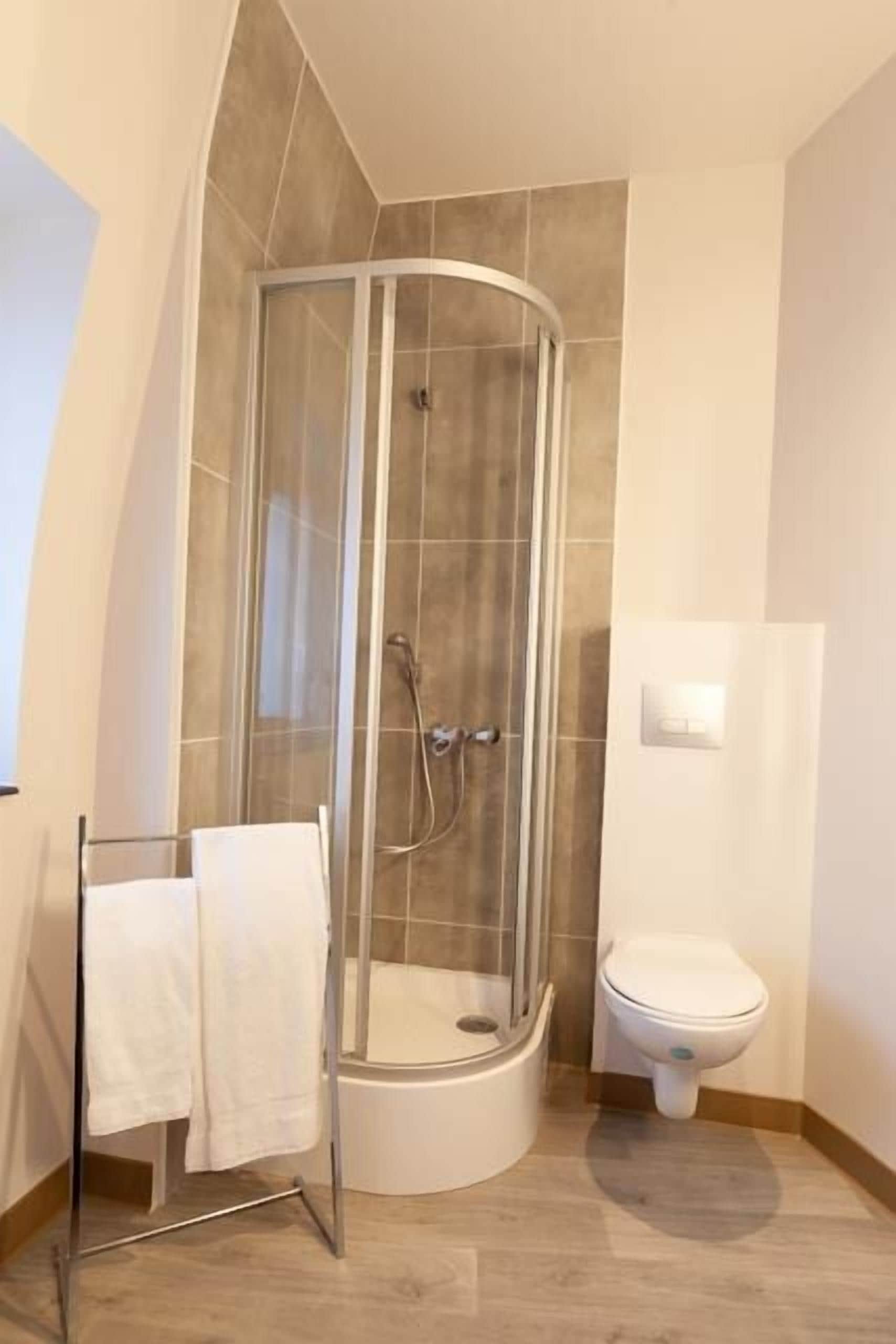 Un baño con ducha de vidrio, inodoro y toallero con dos toallas.