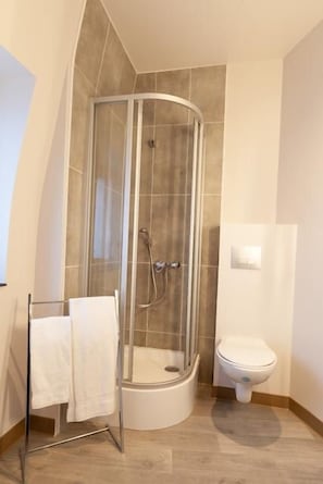 A bathroom with a glass-enclosed shower, a toilet, and a towel rack with two towels. - HNG Hotel Nancy Gare (Nancy)