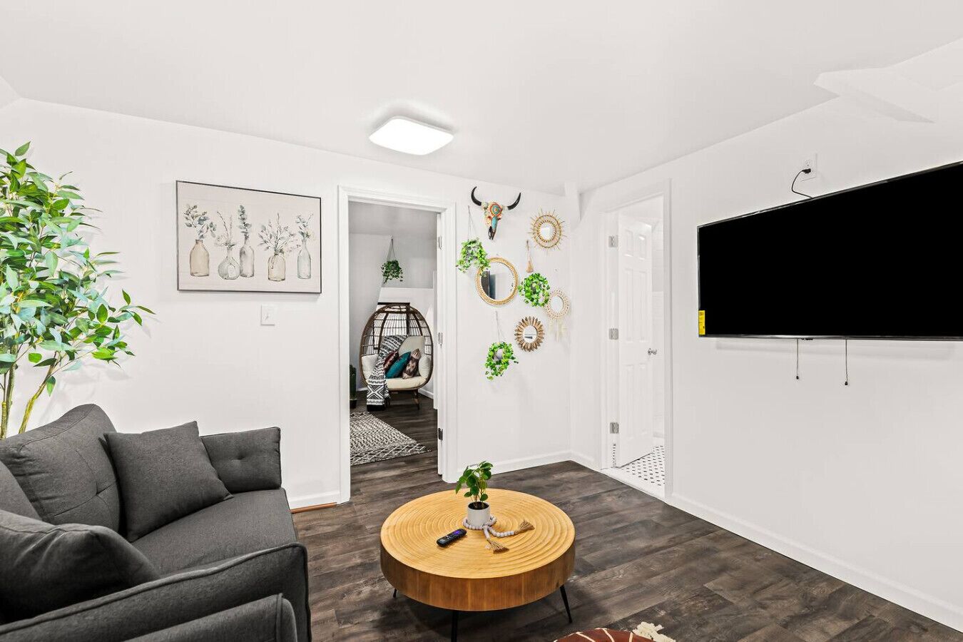 Un salon moderne avec un canapé gris, une table basse ronde en bois et un téléviseur fixé au mur.