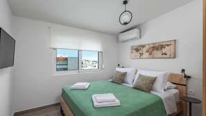 A bedroom with a bed, a window, an air conditioning unit, a world map, and a small table. - Sky High Loft Apartment (Rodos)
