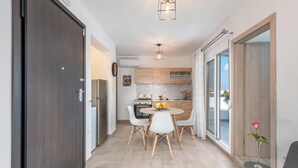A modern kitchen with a dining area, wooden cabinets, a round table, and a small side table with a vase. - Sky High Loft Apartment (Rodos)
