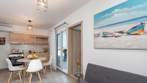 A modern kitchen with wooden cabinets, a dining area with a round table and chairs, a grey sofa, and a beach painting on the wall. - Sky High Loft Apartment (Rodos)