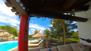 Een zwembadgedeelte met een houten pergola, ligstoelen en een rieten parasol.