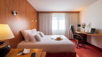A hotel room with a bed, a desk, a lamp, a laptop, and a telephone.