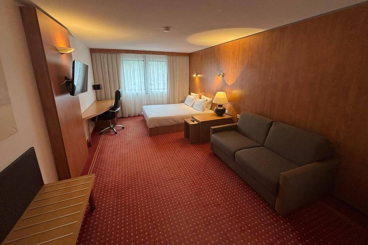 Una habitación de hotel con cama, escritorio, silla, sofá y televisor.