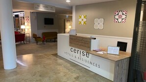 A reception desk labeled 'Cerisé Hotels & Residences' with a modern design, a seating area with a sofa and chairs, and a wall with decorative art pieces. - CERISE Bordeaux Mérignac Aéroport (Merignac)