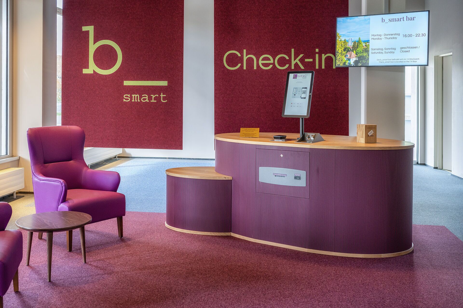 A reception area with a check-in counter, a purple chair, and a sign indicating the b_hotel's smart bar.