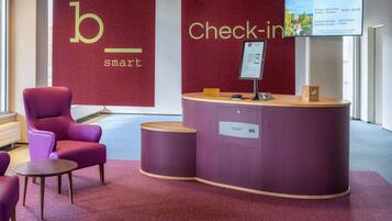 A reception area with a check-in counter, a purple chair, and a sign indicating the b_hotel's smart bar.