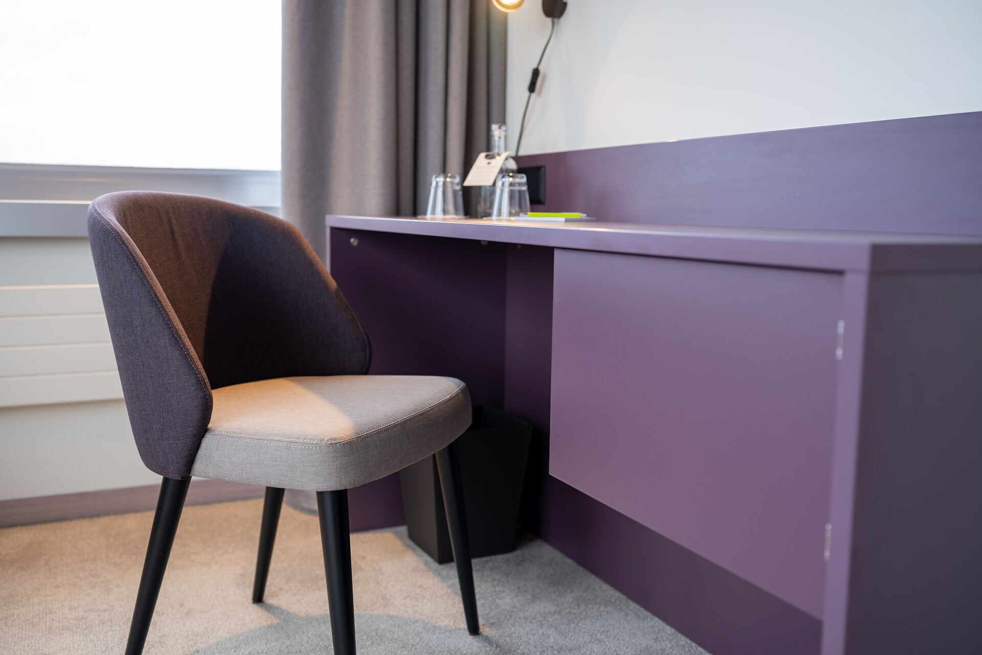 Una silla con asiento y respaldo acolchados, ubicada frente a un escritorio morado con un estante pequeño.