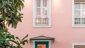 Un bâtiment rose avec une porte bleue, des fenêtres blanches et une petite terrasse avec une table et des chaises.