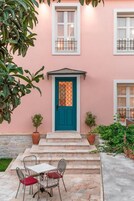 Un edificio rosa con puerta azul, ventanas blancas y un pequeño patio con mesa y sillas.