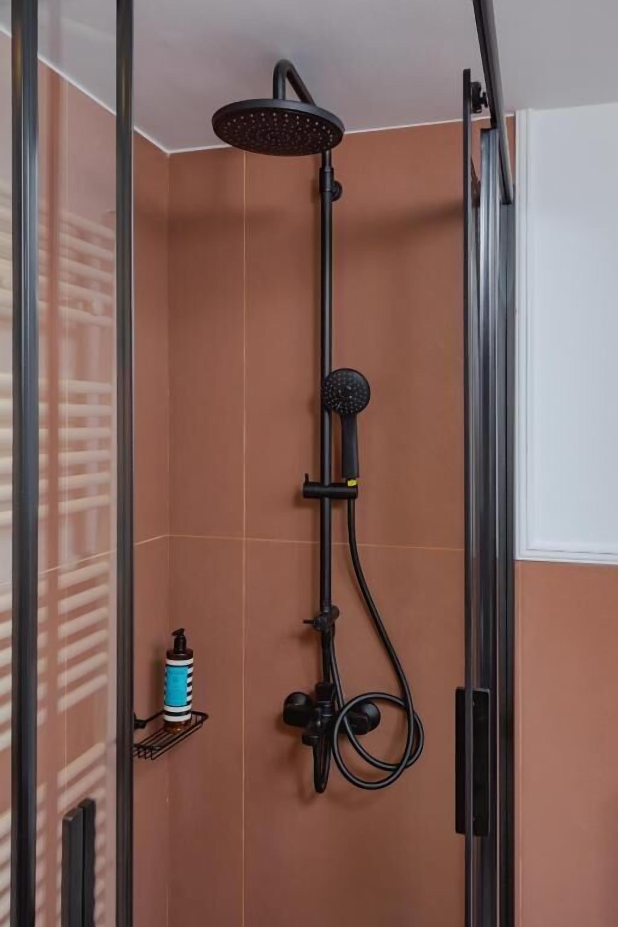 A shower with a handheld showerhead, a wall-mounted faucet, and a soap dispenser on a shelf.