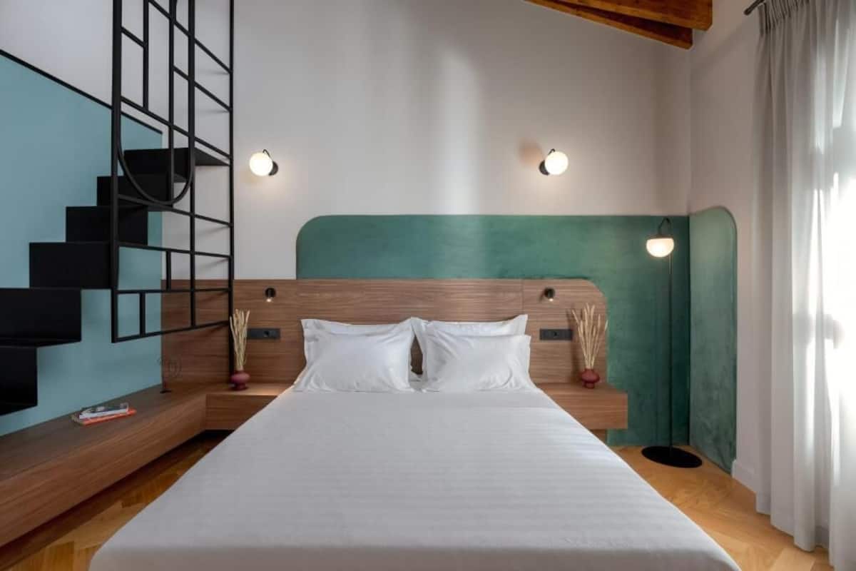 Een moderne hotelkamer met een groot bed, een houten hoofdeinde en een trap met een zwarte leuning.
