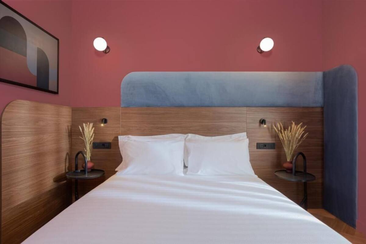 Een netjes opgemaakt bed met witte lakens, een houten hoofdbord en twee nachtkastjes met lampen en decoratieve planten.