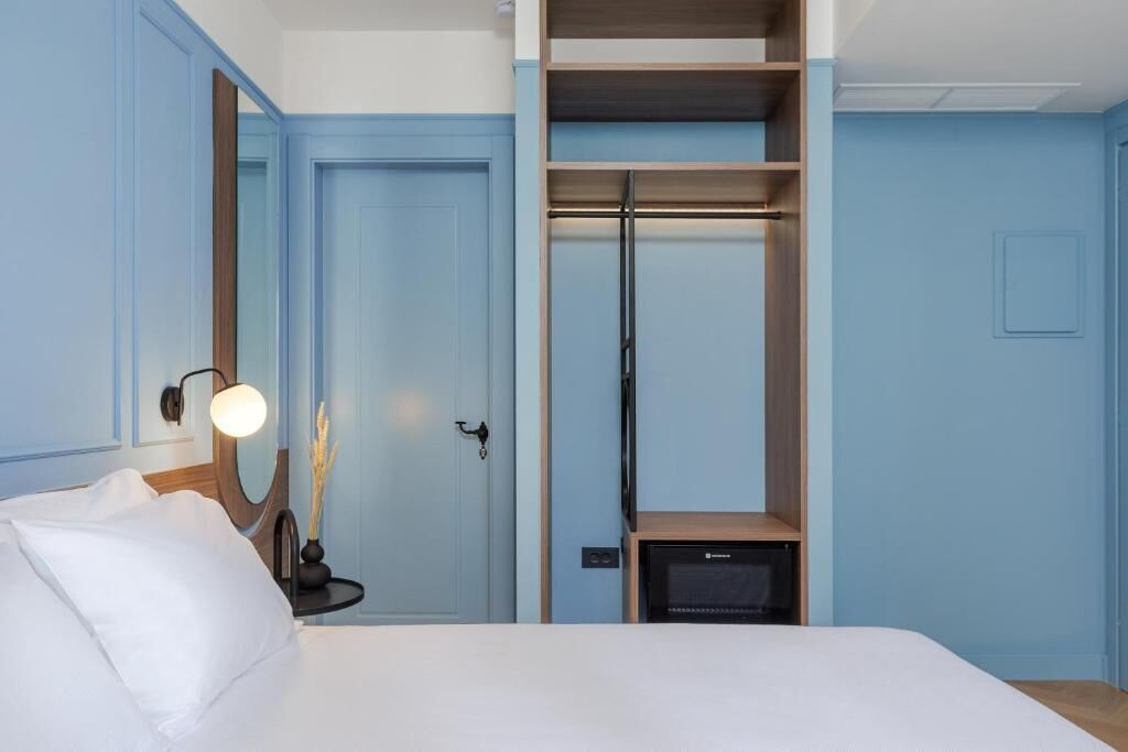 Una habitación de hotel con cama, armario, espejo y una mesita de noche con lámpara.