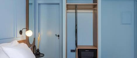 Una habitación de hotel con cama, armario, espejo y una mesita de noche con lámpara.